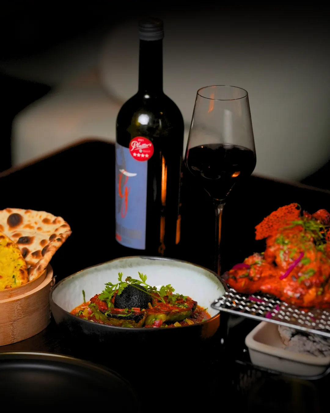 Tandoori chicken, a stuffed chilli curry and naan beside a bottle of red wine.
