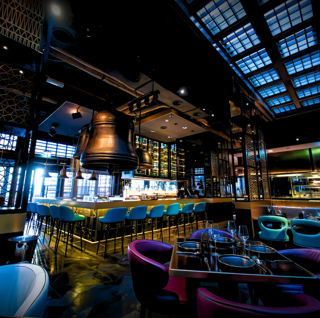 The dining room under a glass skylight, with plum velvet chairs, the bar and brass bells.